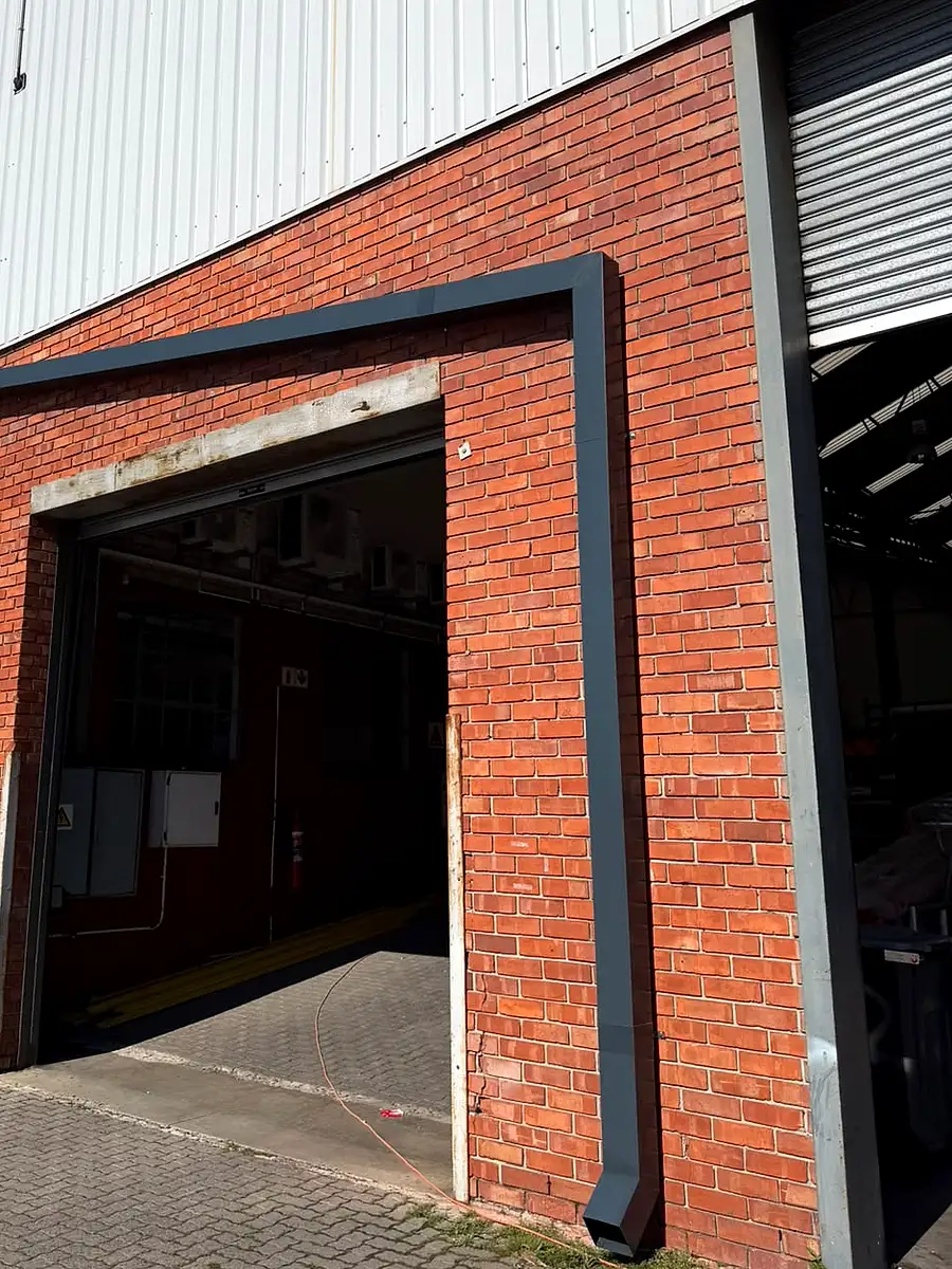 New charcoal downpipe running around a loading door on the red-brick front of an industrial unit